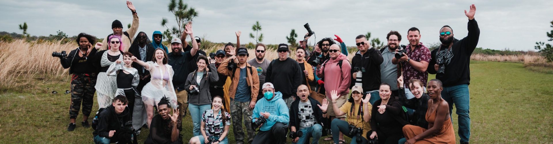 A diverse group of photographers posing together in a natural setting with cameras.
